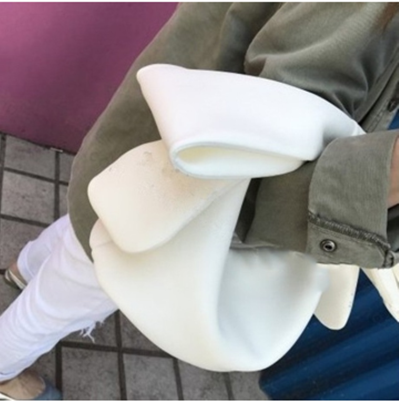 Person in olive jacket and white jeans comfortably holding a white Belle Bow Bag in the crook of their elbow