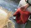 Person wearing silver shoes and beige pants casually holding a red Belle Bow Bag next to frayed wicker mat