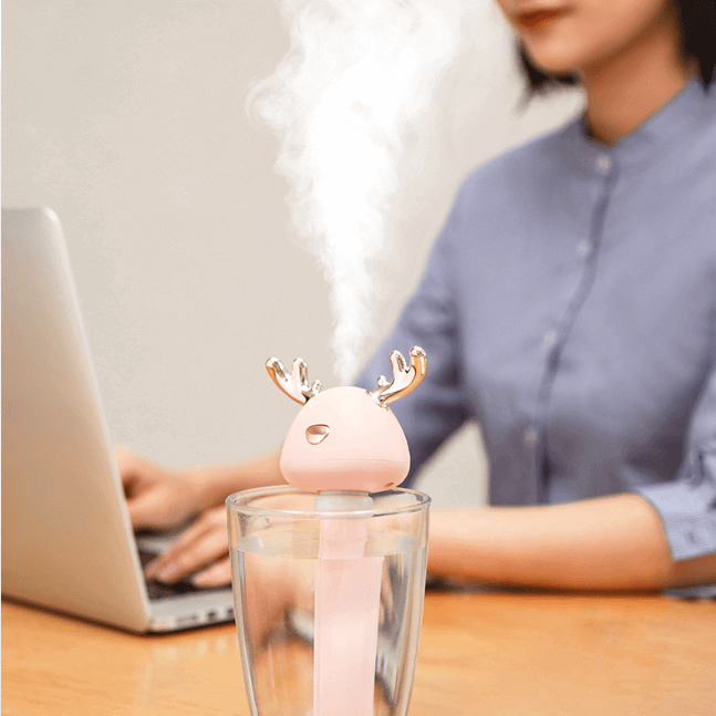 Pink Ava portable humidifier creating mist on study table - girl in background on laptop
