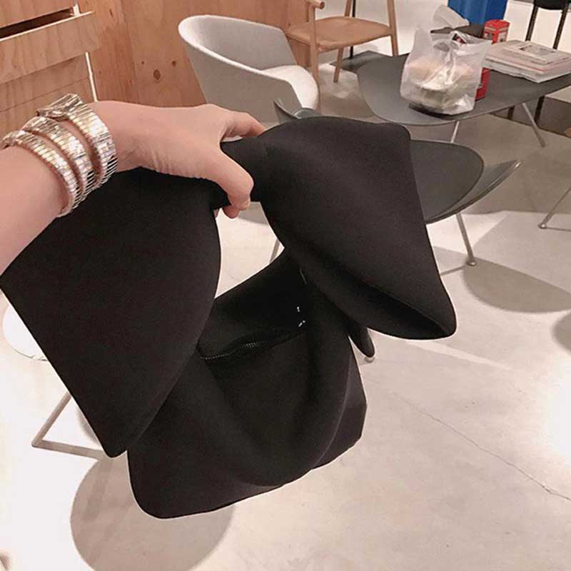 Hand holding a black Belle Bow Bag, showing oversized bow. Wrist adorned in elaborate gold bracelets 