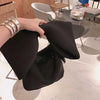 Hand holding a black Belle Bow Bag, showing oversized bow. Wrist adorned in elaborate gold bracelets 