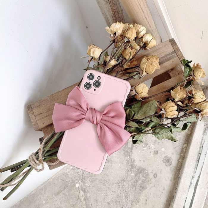 Matte Minimalist Paris Pink Belle Bow Case showing back of phone and linen bow, set against a farmhouse crate with a bouquet of aging white roses