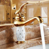 Load image into Gallery viewer, Coco glam faucet - 1 / short - opulence and gold glam galore. The gold faucet accented by white ceramic core  set on brown marble sink looks warm and tastefully decorated. Windows, chandelier, even shelving all reflect shades of gold for an indulgent yet classy statement 