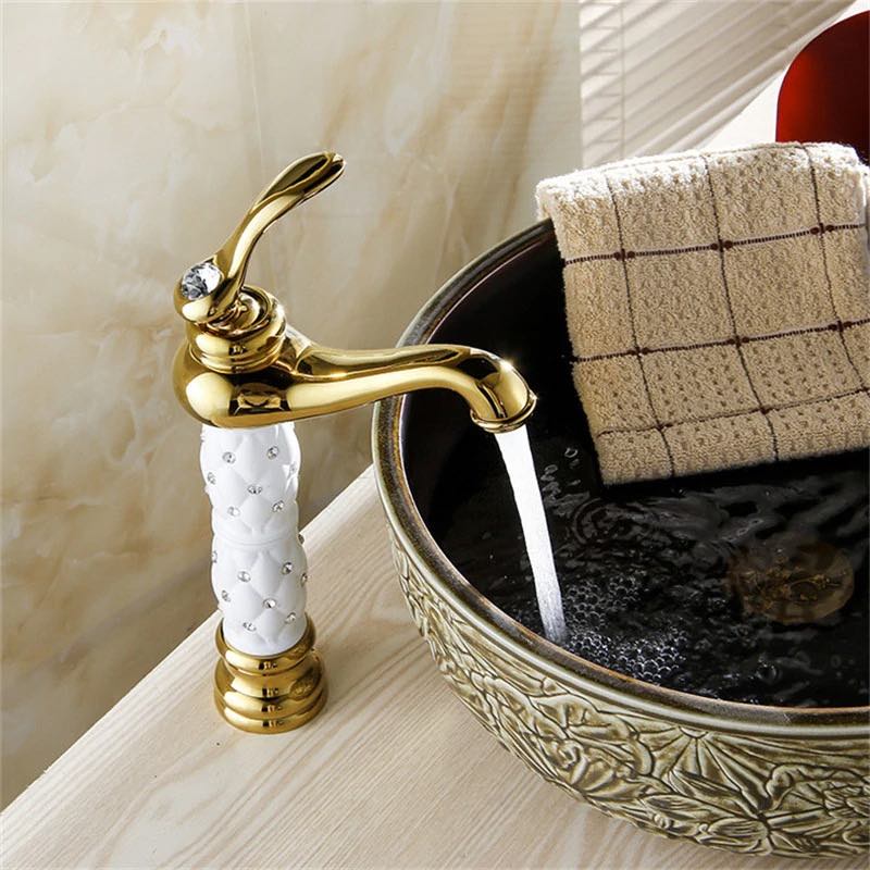 Coco glam faucet - 1 / tall - home & office. Beautiful example of the tall faucet. White ceramic core supports gold tap and base. Aerated water in a controlled stream bubbles as it hits the elaborate elevated sink on an unpolished white wood counter.