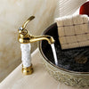 Coco glam faucet - 1 / tall - home & office. Beautiful example of the tall faucet. White ceramic core supports gold tap and base. Aerated water in a controlled stream bubbles as it hits the elaborate elevated sink on an unpolished white wood counter.