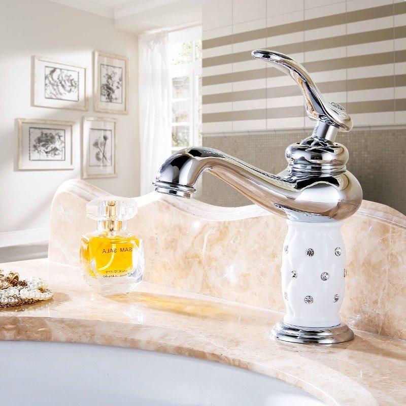 Coco glam faucet - short white ceramic core with chrome silver tap mounted on beige marble countertop. Background shows beige and white walls open window with white curtains, sunlight falling on pictures mounted on the wall. 